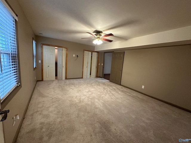 unfurnished bedroom featuring carpet floors, ceiling fan, and multiple closets
