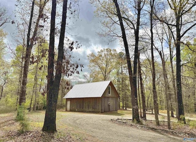 view of side of home featuring a garage, an outdoor structure, driveway, metal roof, and a wooded view