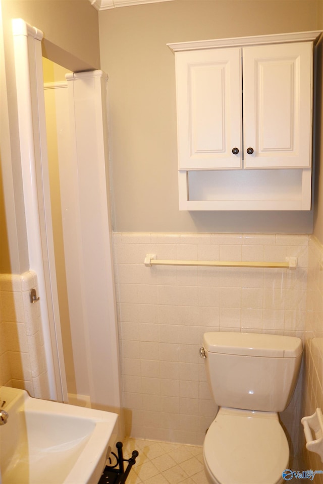 bathroom featuring tile patterned floors, toilet, sink, and tile walls