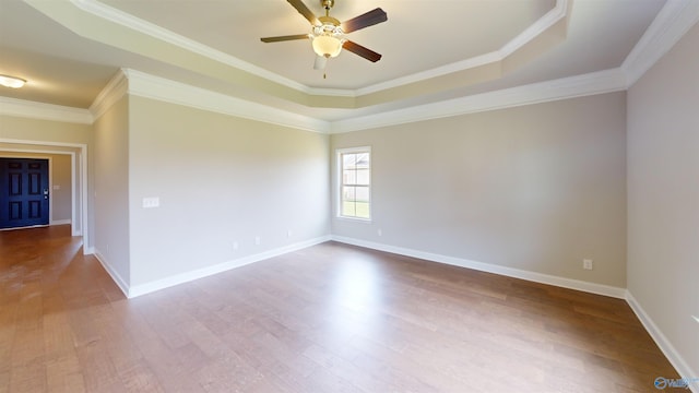 empty room with a tray ceiling, ceiling fan, hardwood / wood-style floors, and ornamental molding