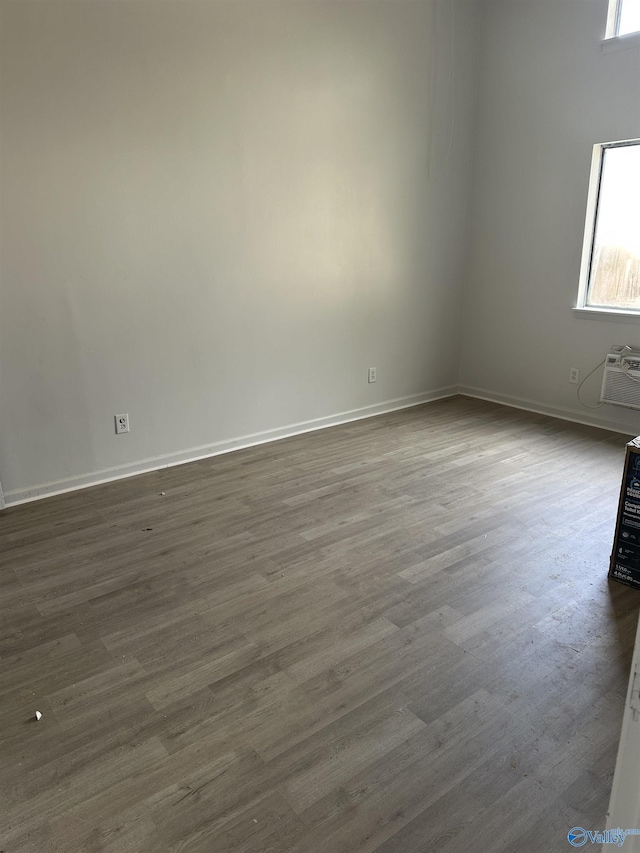 empty room featuring an AC wall unit, baseboards, and dark wood-style floors