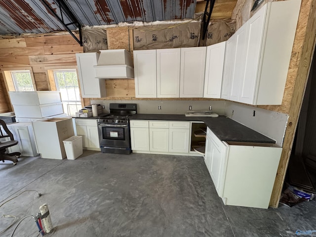 kitchen with white cabinets, dark countertops, premium range hood, unfinished concrete flooring, and stainless steel gas stove