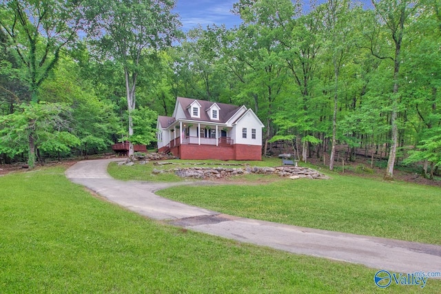 cape cod-style house with a view of trees, driveway, covered porch, and a front yard
