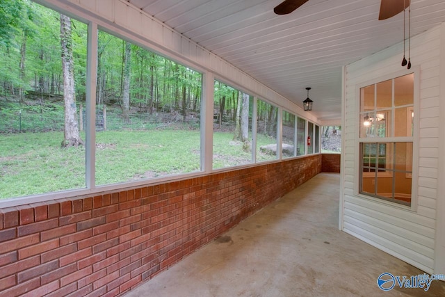 unfurnished sunroom featuring a wooded view and a ceiling fan