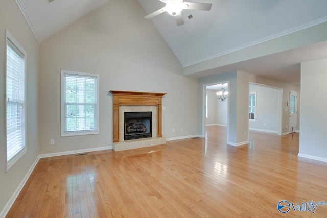 unfurnished living room with visible vents, high vaulted ceiling, a tile fireplace, light wood finished floors, and ceiling fan with notable chandelier