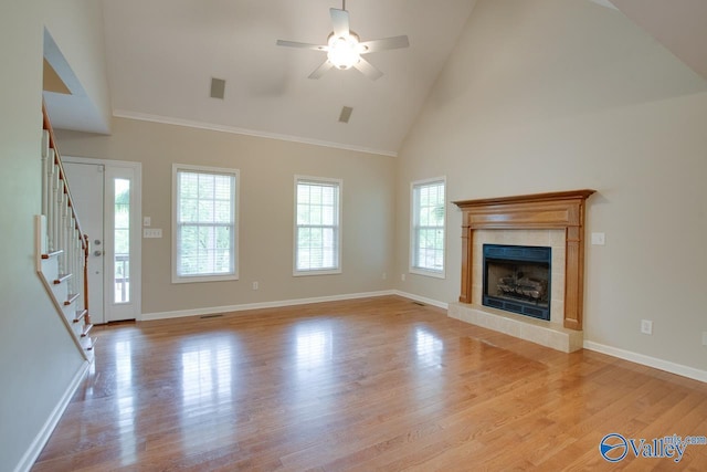 unfurnished living room featuring ceiling fan, a tiled fireplace, stairway, high vaulted ceiling, and light wood-style floors