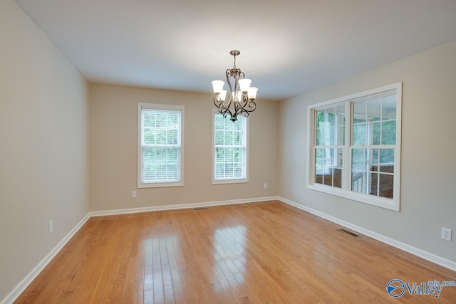 empty room with baseboards, visible vents, light wood-type flooring, and a chandelier