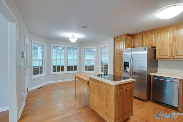 kitchen featuring appliances with stainless steel finishes, light countertops, a center island, baseboards, and light wood-type flooring