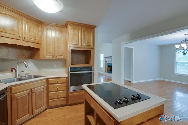 kitchen featuring a sink, stainless steel appliances, light wood-type flooring, and a notable chandelier