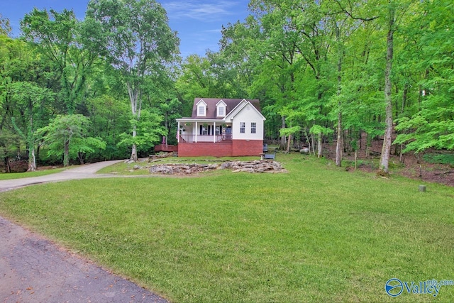 view of front of home with a forest view, driveway, brick siding, and a front yard