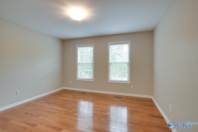 empty room featuring baseboards, visible vents, and light wood finished floors