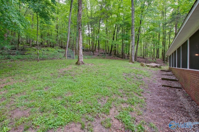 view of yard featuring a sunroom and a wooded view