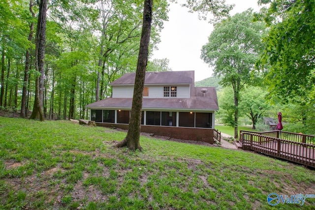 rear view of property featuring a lawn, a sunroom, a deck, and brick siding