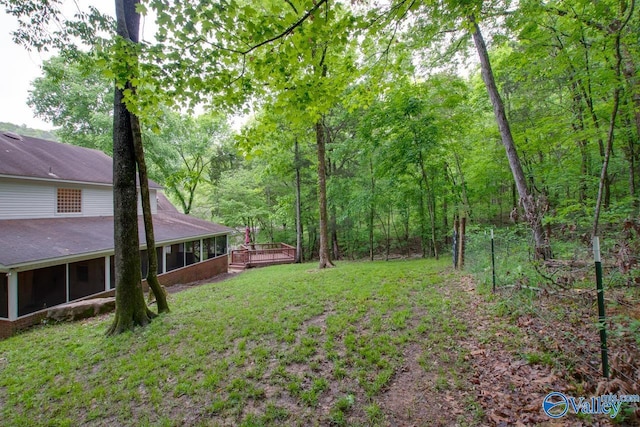 view of yard featuring a wooden deck, a sunroom, and a forest view