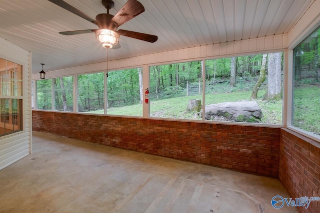 unfurnished sunroom featuring a ceiling fan, brick wall, and unfinished concrete floors