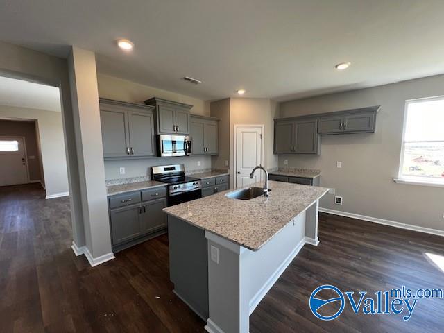 kitchen with appliances with stainless steel finishes, dark hardwood / wood-style flooring, sink, gray cabinets, and an island with sink