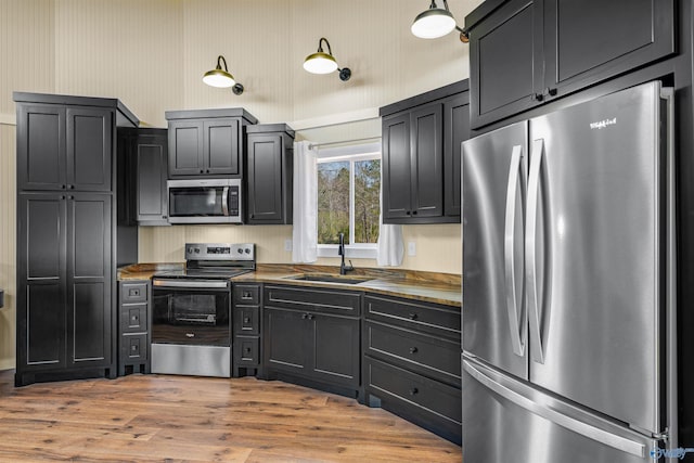 kitchen featuring a sink, dark cabinetry, appliances with stainless steel finishes, light wood-type flooring, and wallpapered walls