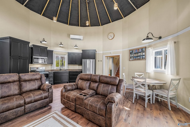 living area featuring a towering ceiling, a wall mounted air conditioner, stairway, and wood finished floors