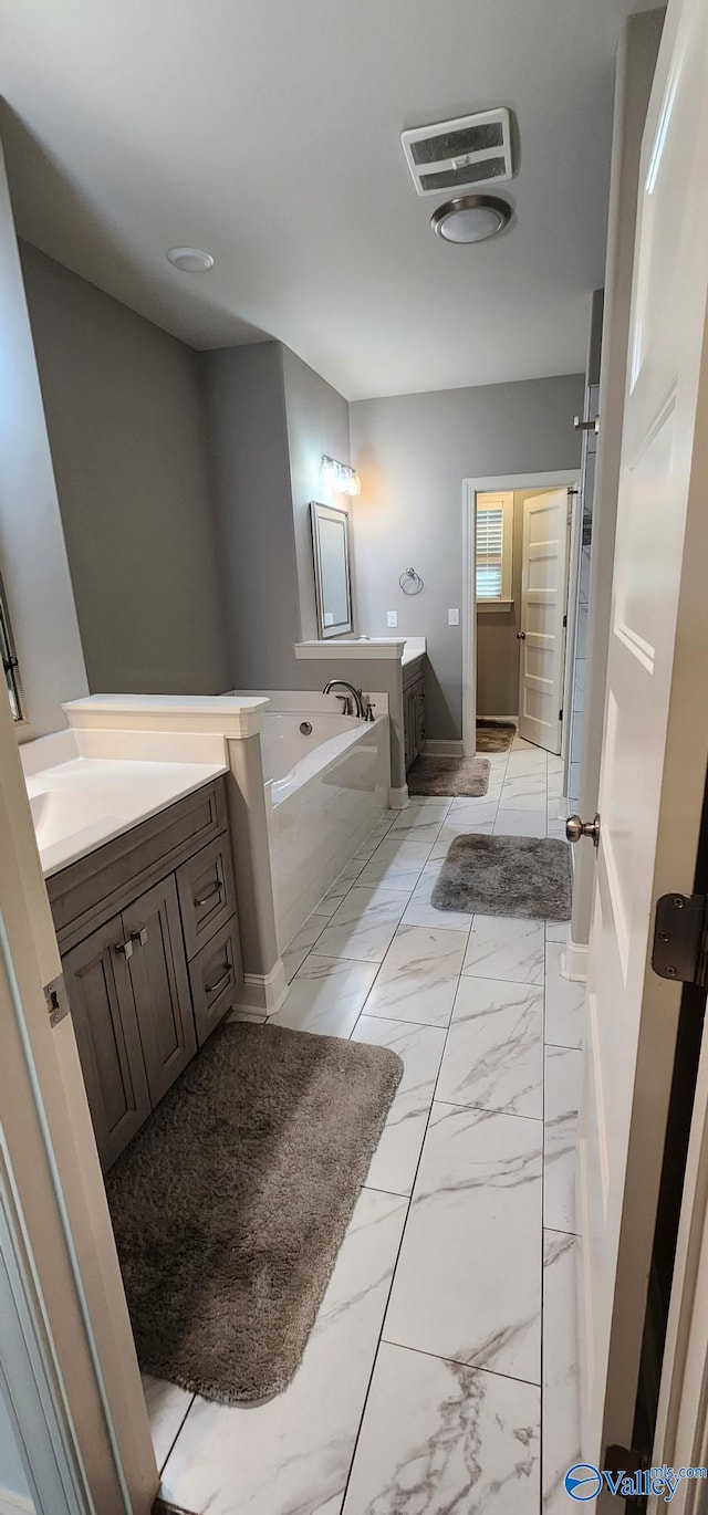 bathroom featuring marble finish floor, visible vents, a garden tub, and vanity