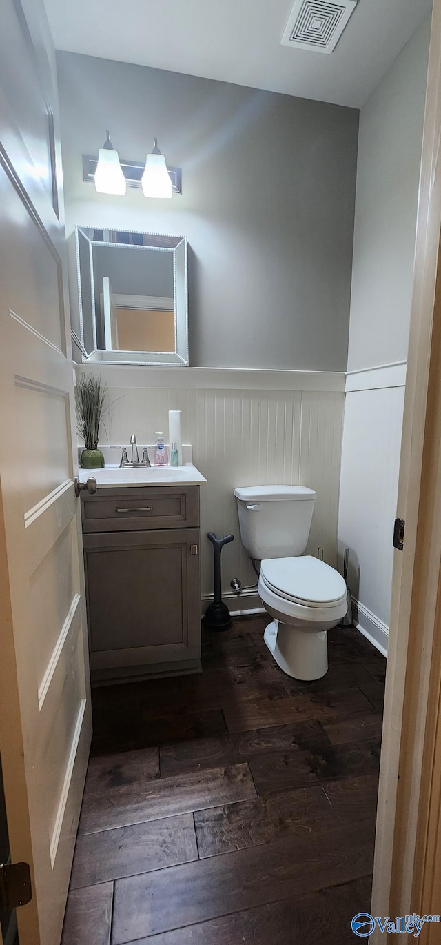 half bath featuring wainscoting, visible vents, hardwood / wood-style floors, and toilet