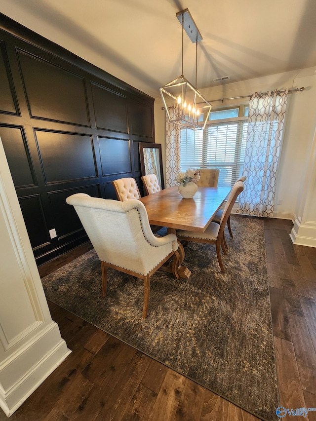 dining room with a chandelier, dark wood-type flooring, and a decorative wall