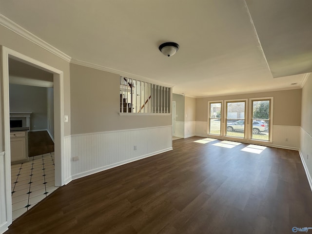 empty room with a wainscoted wall, ornamental molding, stairway, and wood finished floors