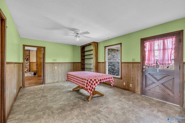 game room featuring a textured ceiling, wood walls, and ceiling fan