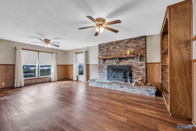 unfurnished living room featuring a textured ceiling, wood walls, hardwood / wood-style flooring, and ceiling fan