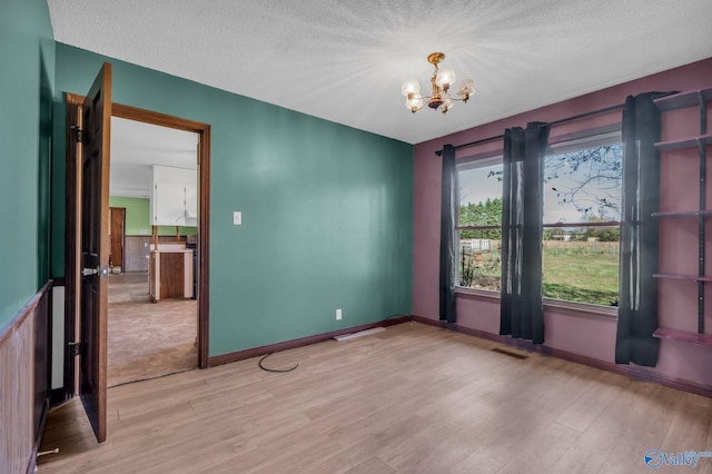 unfurnished room featuring light wood-type flooring, a textured ceiling, and a chandelier