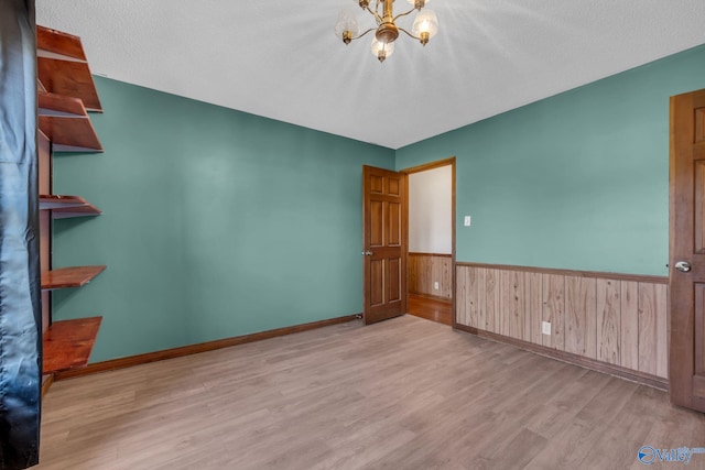 spare room featuring a textured ceiling, wooden walls, light wood-type flooring, and a notable chandelier