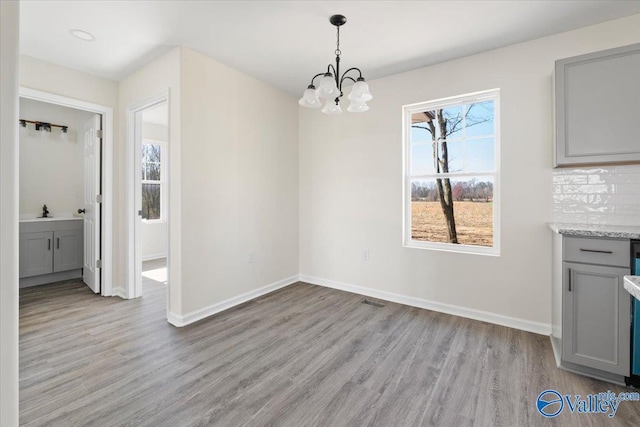 unfurnished dining area featuring sink, light hardwood / wood-style floors, and a notable chandelier