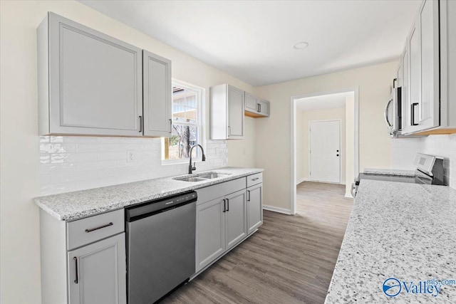 kitchen with sink, stainless steel appliances, light stone countertops, hardwood / wood-style floors, and decorative backsplash