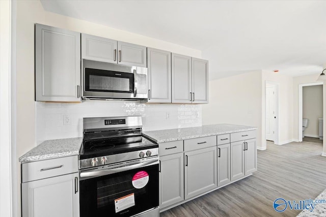 kitchen with tasteful backsplash, gray cabinets, stainless steel appliances, light stone countertops, and light hardwood / wood-style floors