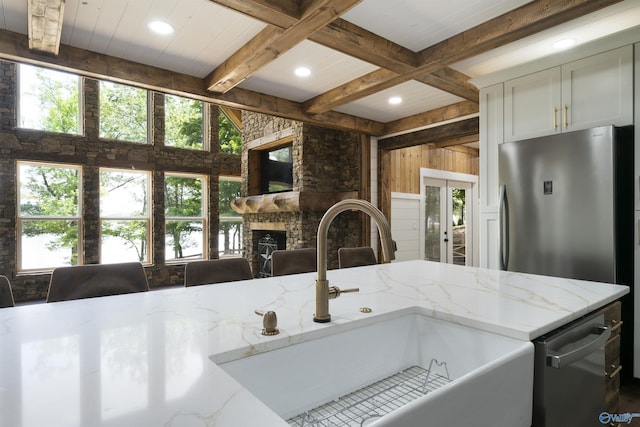 691 County Road 106, Leesburg, AL 35983 - kitchen featuring healthy amount of natural light, appliances with stainless steel finishes, beam ceiling, a stone fireplace, and light stone counters