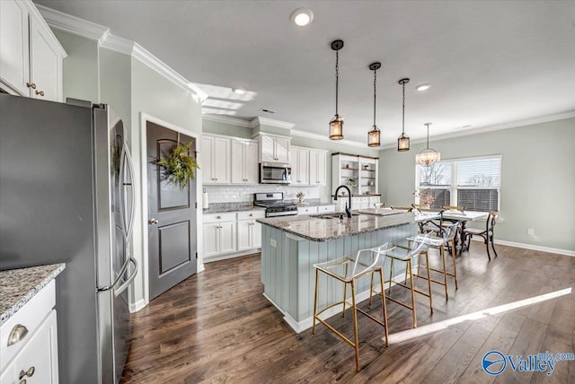 kitchen featuring light stone countertops, appliances with stainless steel finishes, a center island with sink, white cabinets, and a breakfast bar area