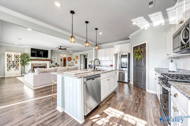 kitchen with stainless steel appliances, white cabinetry, a kitchen island with sink, and light stone counters