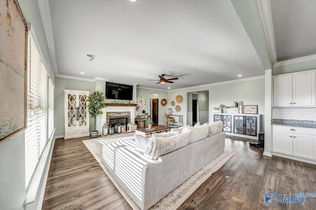 unfurnished living room with wood-type flooring, a stone fireplace, ceiling fan, and ornamental molding