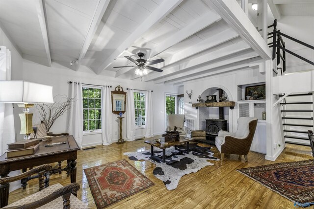 living room with a wood stove, light hardwood / wood-style floors, beamed ceiling, and ceiling fan