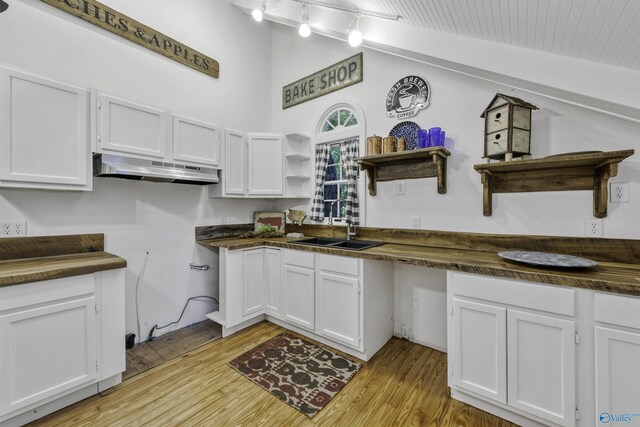 kitchen featuring sink, lofted ceiling with skylight, white cabinetry, and light wood-type flooring