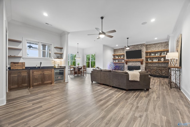 27 Watson Grande Way, Owens Cross Roads, AL 35763 - living area featuring wine cooler, ceiling fan, light wood-style floors, a brick fireplace, and crown molding