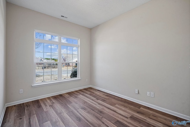 spare room with visible vents, dark wood-style floors, baseboards, and a textured ceiling