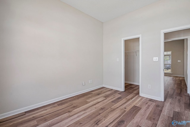 unfurnished bedroom featuring a closet, baseboards, a walk in closet, and wood finished floors