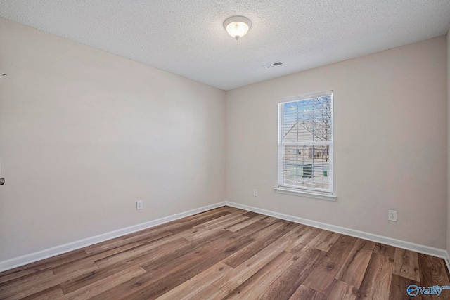 unfurnished room with a textured ceiling, wood finished floors, visible vents, and baseboards