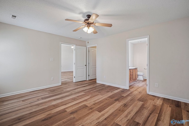 unfurnished bedroom with visible vents, baseboards, ensuite bathroom, a textured ceiling, and light wood-type flooring