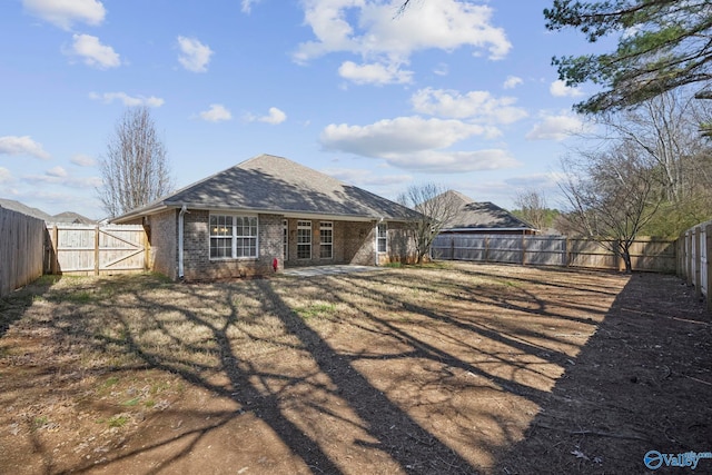 back of house with brick siding, roof with shingles, a fenced backyard, and a gate