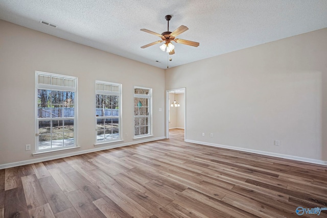 spare room with visible vents, baseboards, ceiling fan with notable chandelier, wood finished floors, and a textured ceiling