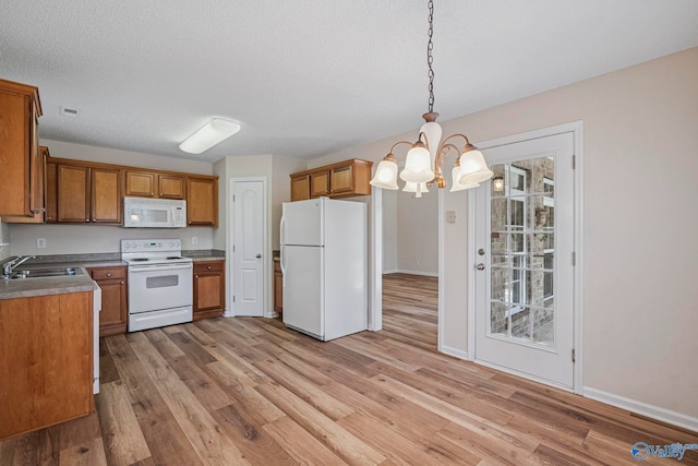 kitchen featuring white appliances, a sink, light wood-style floors, decorative light fixtures, and brown cabinets