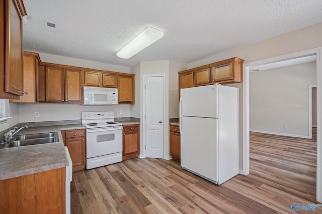 kitchen featuring light wood finished floors, brown cabinetry, white appliances, a textured ceiling, and a sink