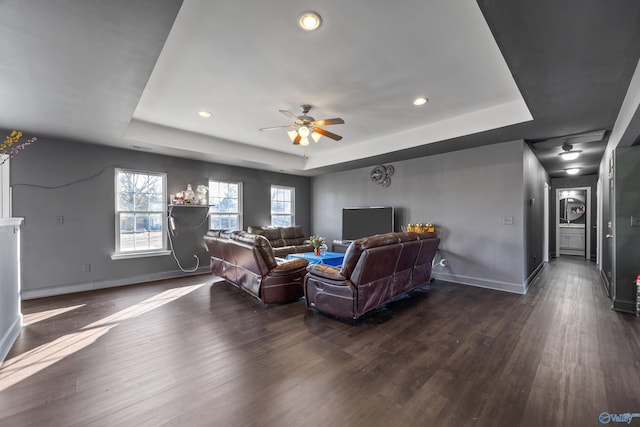 living room featuring a raised ceiling, dark wood-type flooring, and ceiling fan