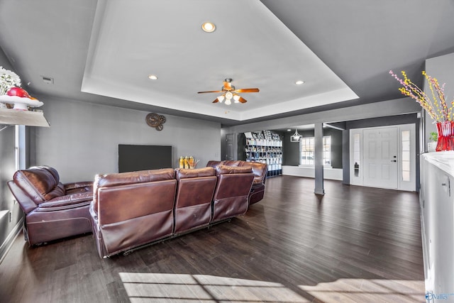 living room featuring dark wood-type flooring, decorative columns, a raised ceiling, and ceiling fan